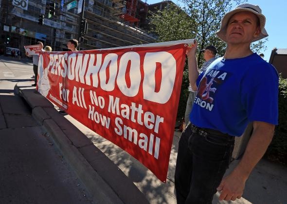 Man holding banner that says "Personhood For All No Matter How Small"