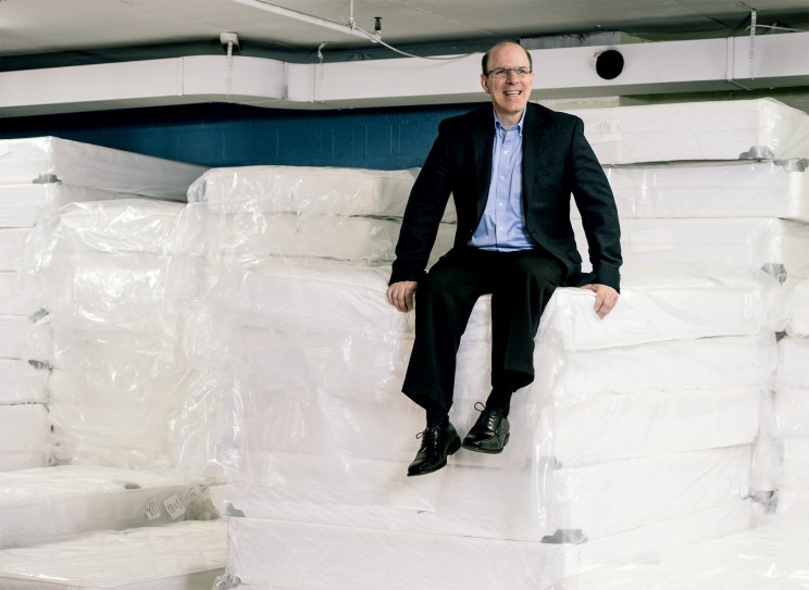 Man sitting on large stacks of mattresses